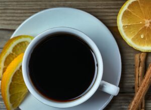 A steaming cup of black coffee served with lemon slices on a wooden surface, highlighting the key ingredients of the Coffee Loophole Recipe.